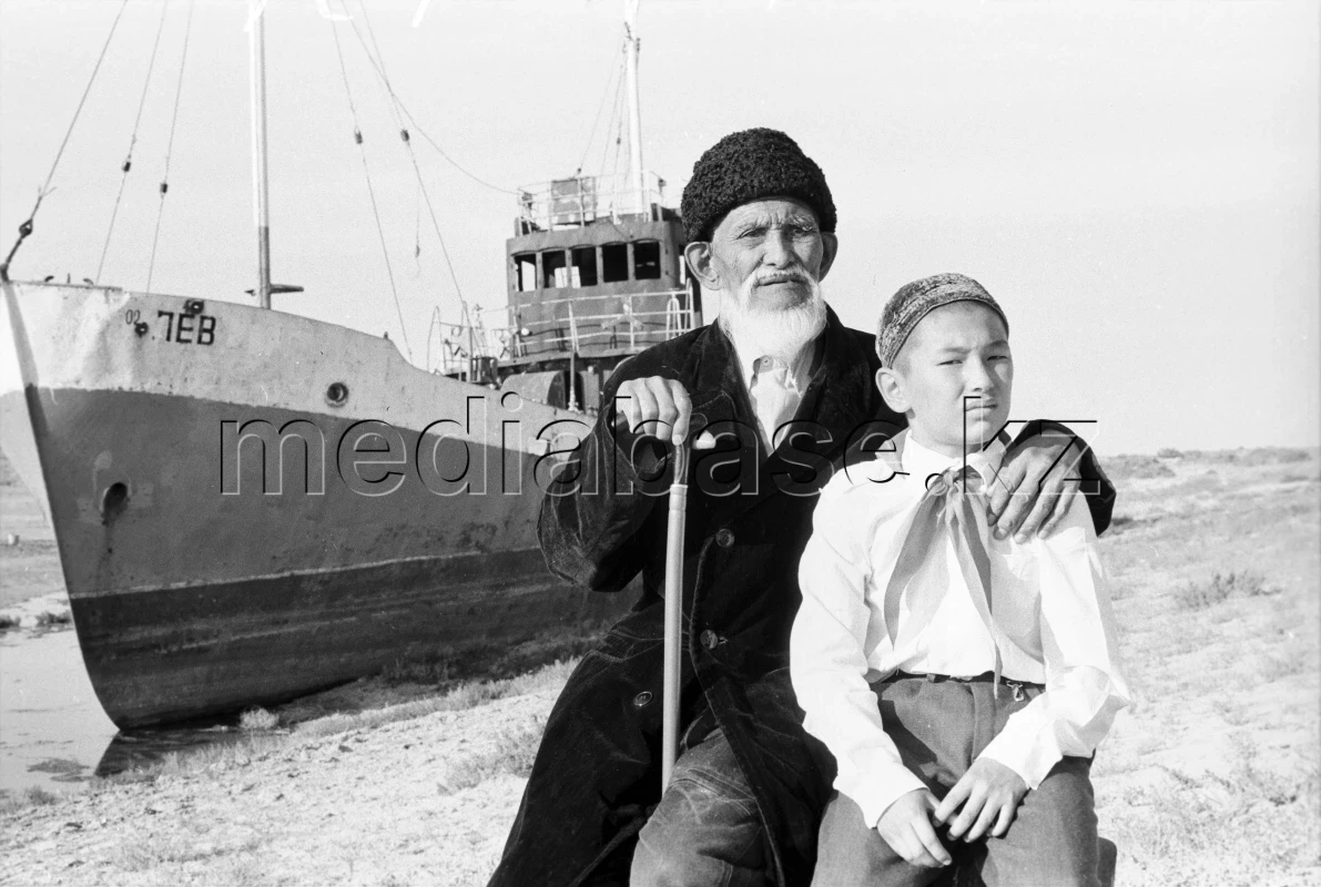 Рыбак Акынгазы Аралбаев с внуком на фоне рыболовного траулера на дне высохшего Арала 1981 год - фото 1