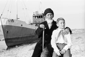 Балықшы Ақынғазы Аралбаев немересімен кеуіп қалған Арал теңізінің түбінде балық аулайтын траулер фонында 1981 жыл - фото 1